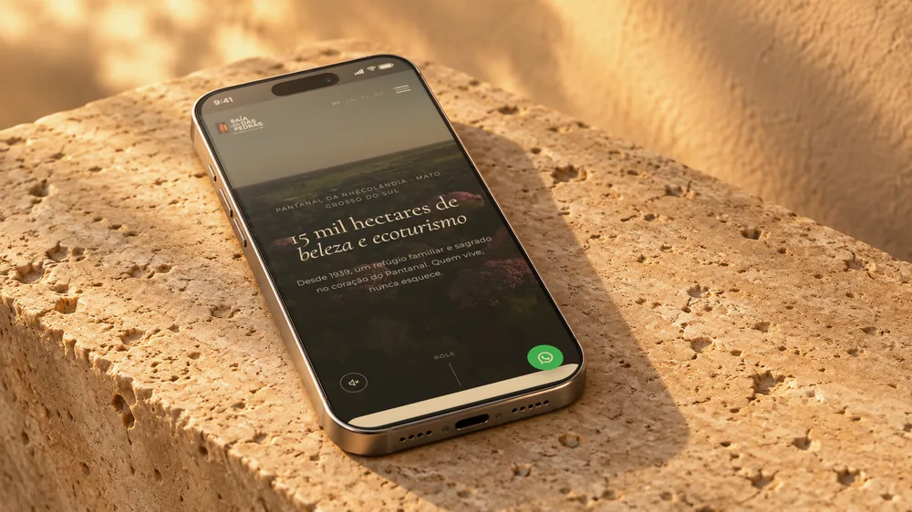 Celular sobre um bloco de pedra exibindo o site da Baía das Pedras